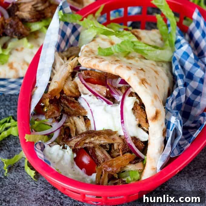 A vibrant plate of homemade pork gyros with fresh tzatziki and a drizzle of sweet chili sauce, garnished with herbs.