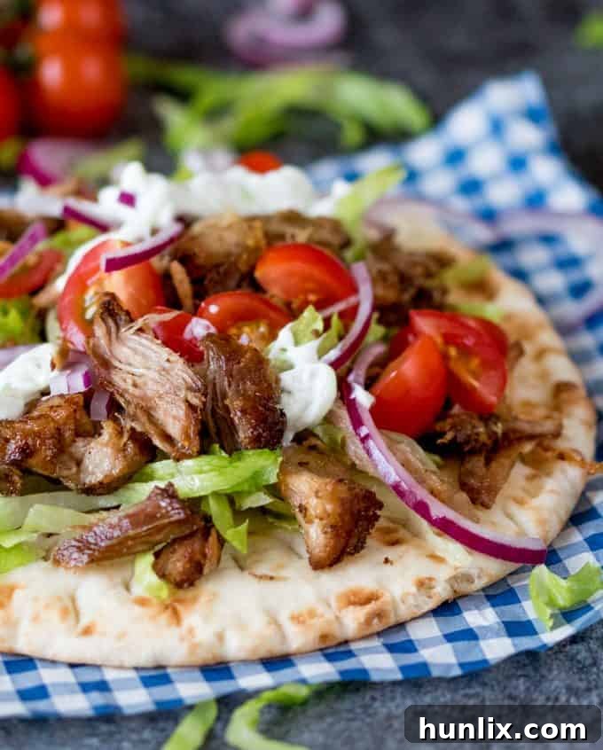 A close-up of an open pita bread filled with pork gyros, tzatziki, and fresh vegetables, ready to be enjoyed.