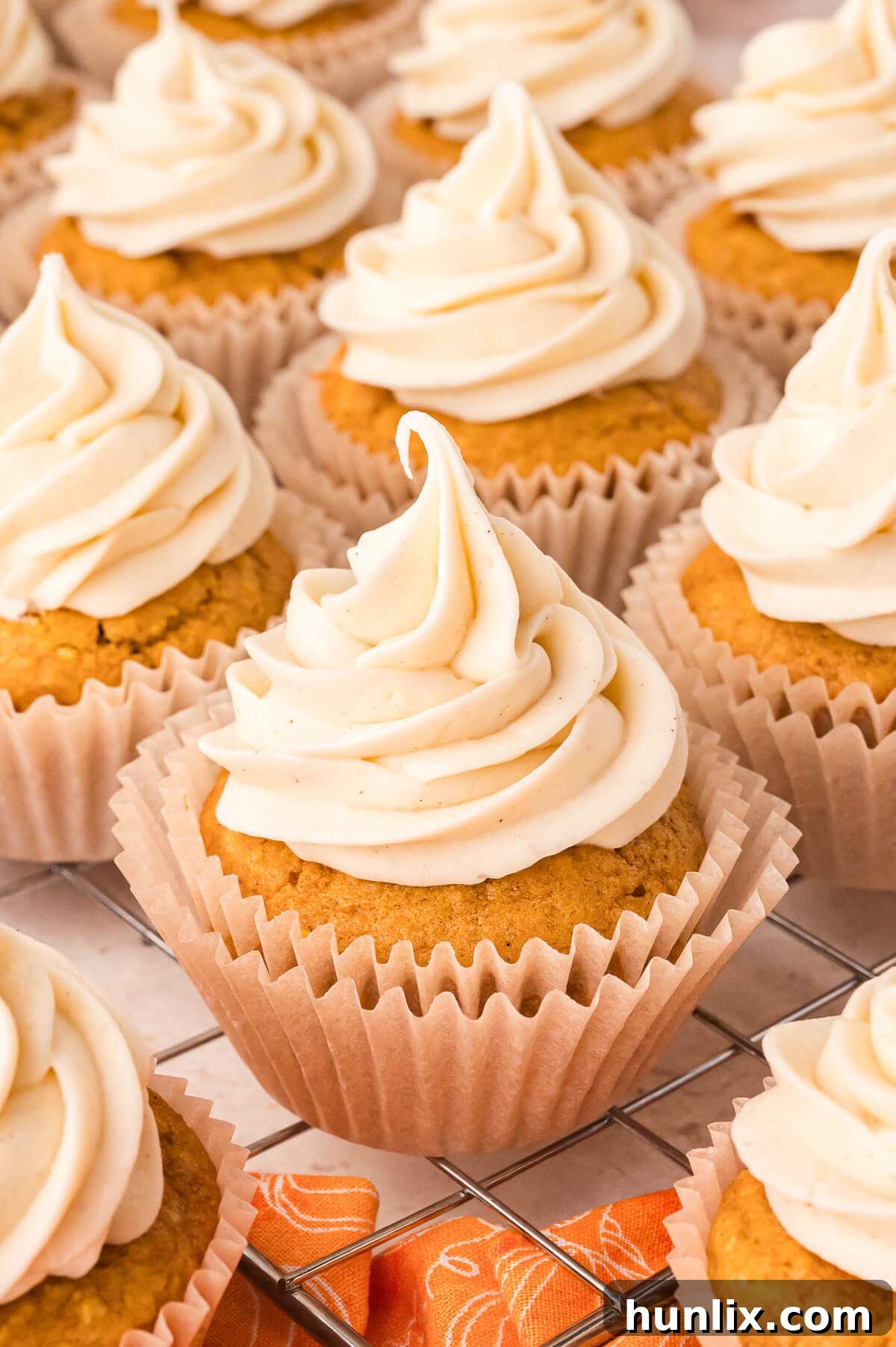 A stunning arrangement of homemade Pumpkin Pie Cupcakes on a sleek wire cooling rack, showcasing their golden crusts, fluffy pumpkin cake, and generous swirls of creamy pumpkin spice buttercream.