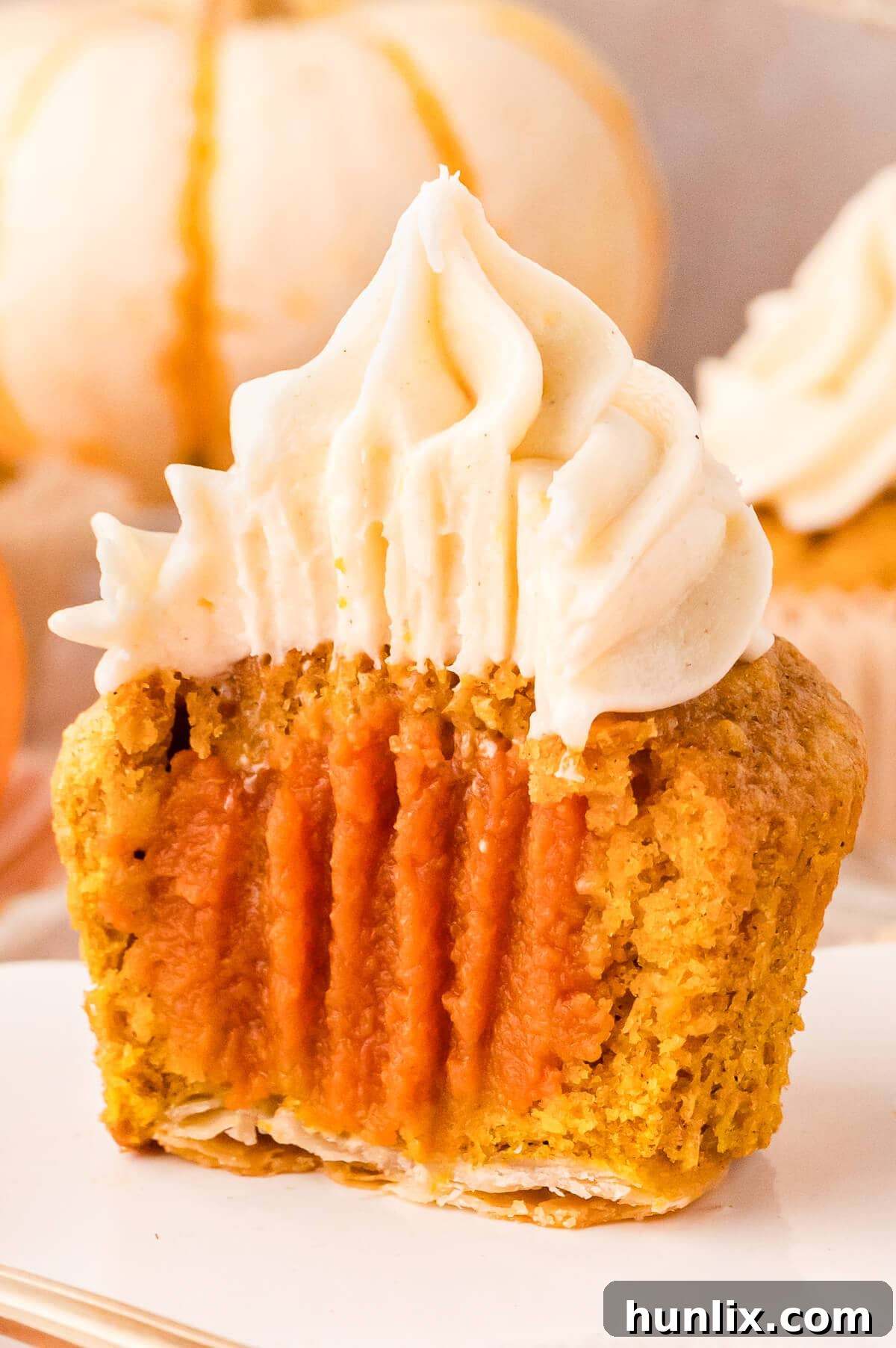 A Pumpkin Pie Cupcake expertly sliced in half on a white plate, revealing the intricate layers of pie crust, pumpkin cake, and the hidden pumpkin pie filling.