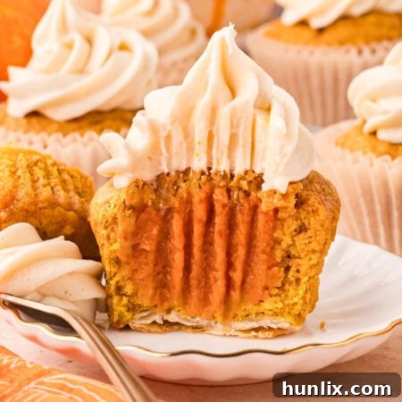 A pumpkin pie cupcake sliced in half on a white plate, showcasing the layers of pie crust, pumpkin cake, and filling.
