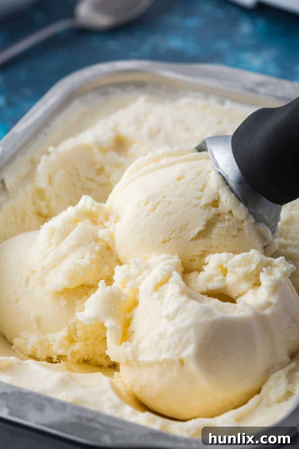 Homemade vanilla ice cream in a tub with an ice cream scoop, ready to be served.