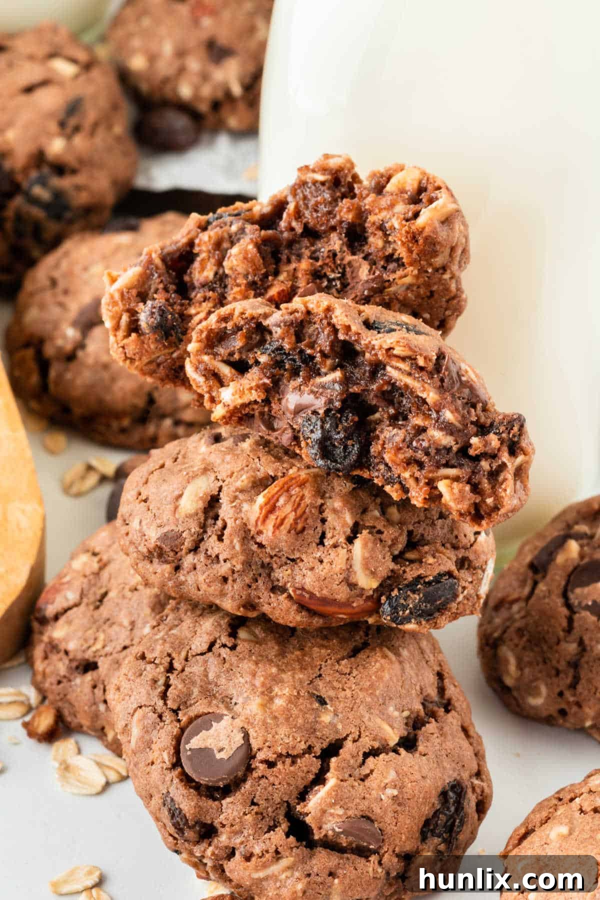 A stack of Cowboy Cookies, with the top cookie having a bite taken out, revealing its chewy interior and rich mix-ins, on a wooden surface.