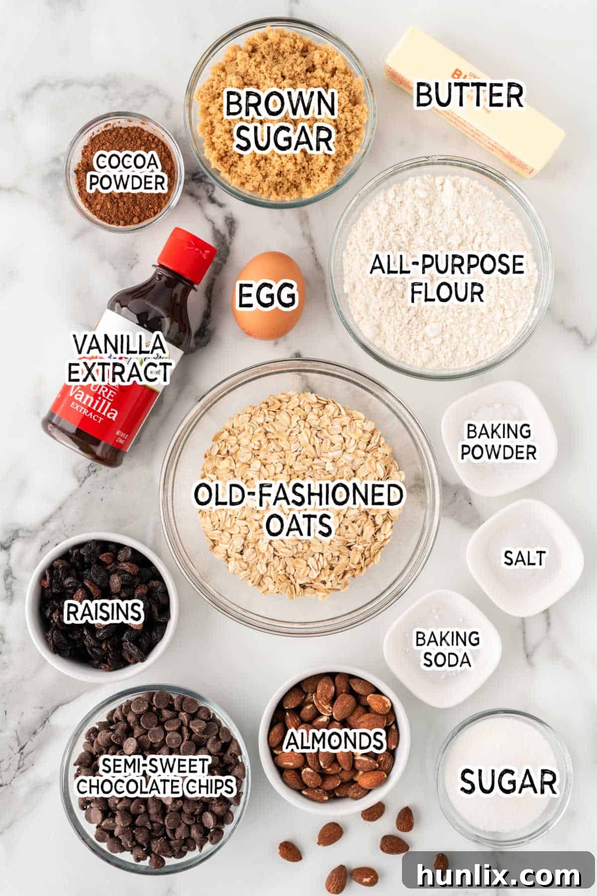 A selection of raw ingredients for Cowboy Cookies, including softened butter, sugars, flour, oats, chocolate chips, raisins, and almonds, neatly arranged on a counter.
