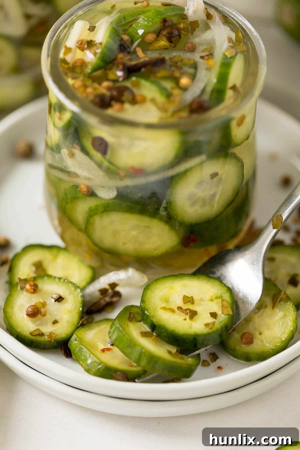 A jar of crisp refrigerator pickles served alongside a plate with a few slices, highlighting their fresh appeal as a snack or side dish.