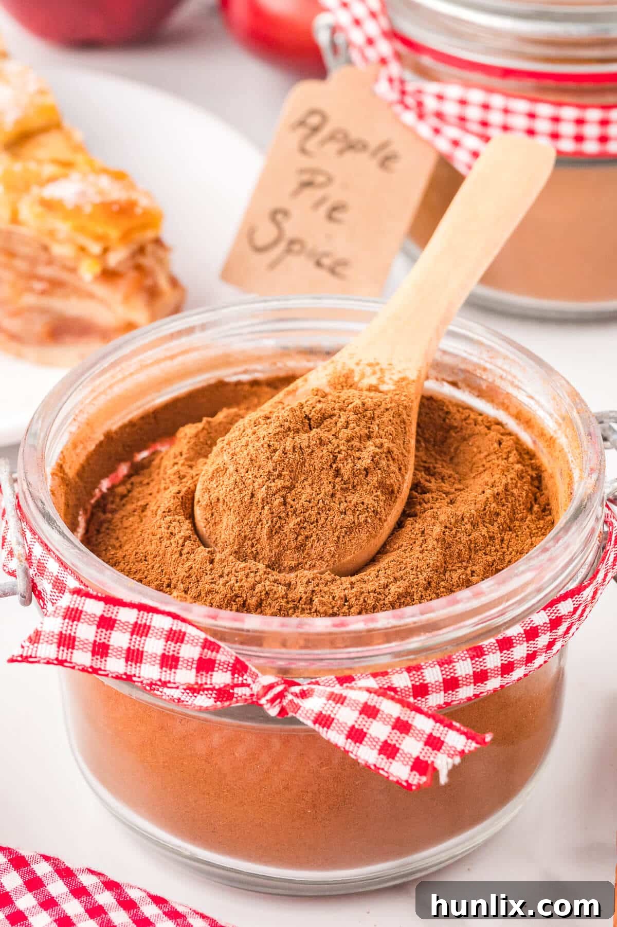 A charming glass jar filled with homemade apple pie spice, accompanied by a small wooden spoon. The warm, inviting colors of the spice hint at the comforting flavors of autumn.