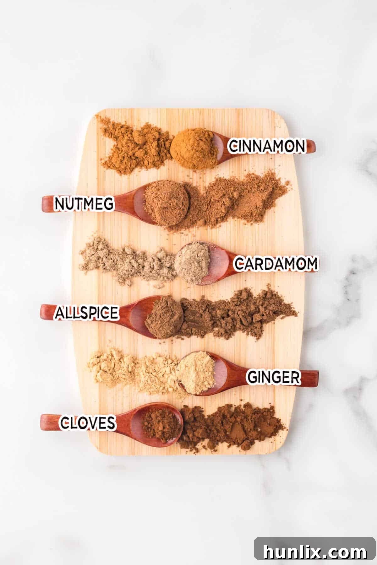 Various individual spices – cinnamon sticks, whole nutmeg, cardamom pods, ginger root, whole cloves, and allspice berries – artfully arranged on a wooden cutting board, ready to be ground for a homemade spice blend.