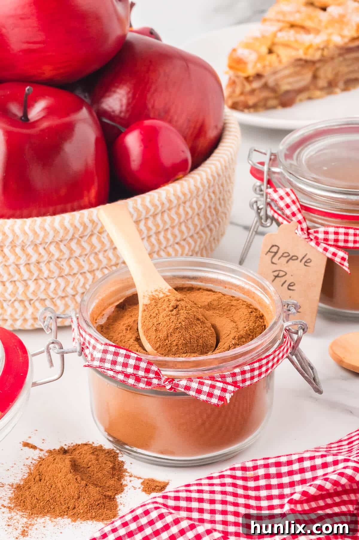 A decorative glass jar, elegantly labeled, holds a fresh batch of homemade apple pie spice, with a wooden spoon carefully placed beside it, inviting the viewer to indulge in fall flavors.