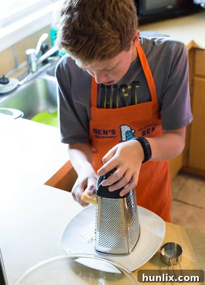 A young boy, Connor, intently grating cheddar cheese for the taco recipe.