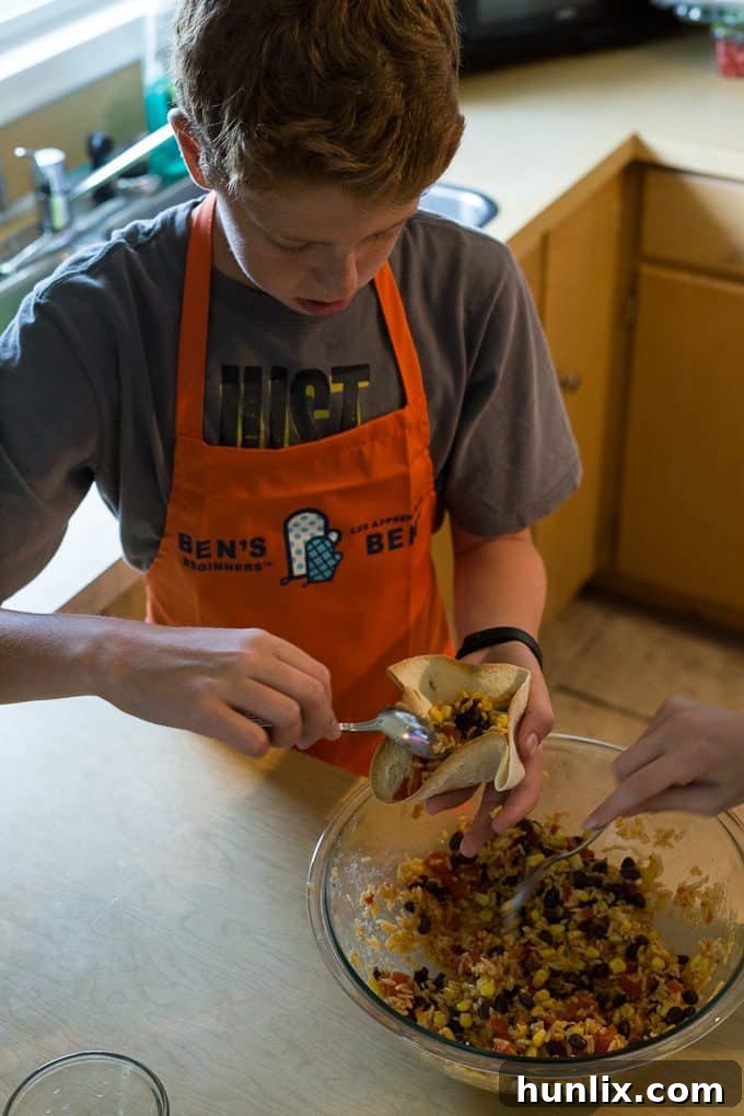 A young chef intently garnishing his black bean and rice open-faced taco with fresh toppings.