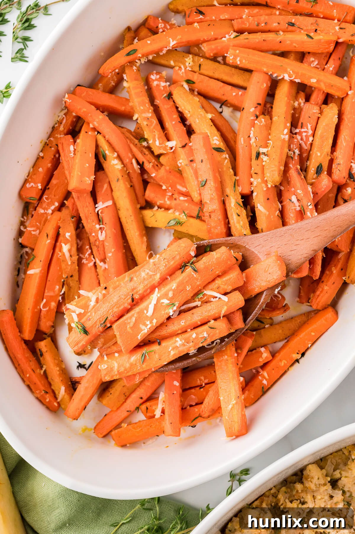 Parmesan roasted carrots in a casserole dish with a wooden spoon.