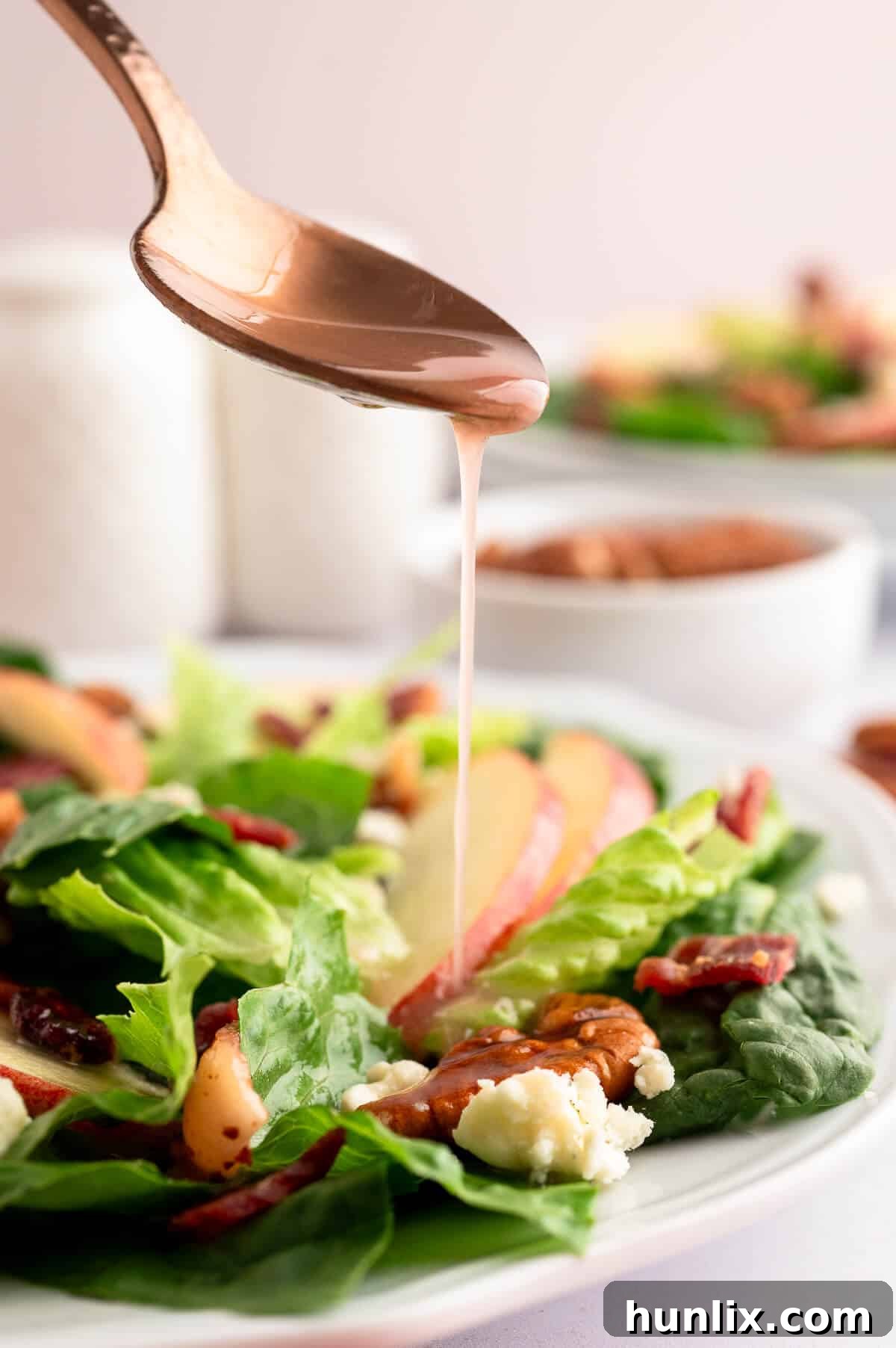 A spoon drizzling bacon vinaigrette over a fall salad.