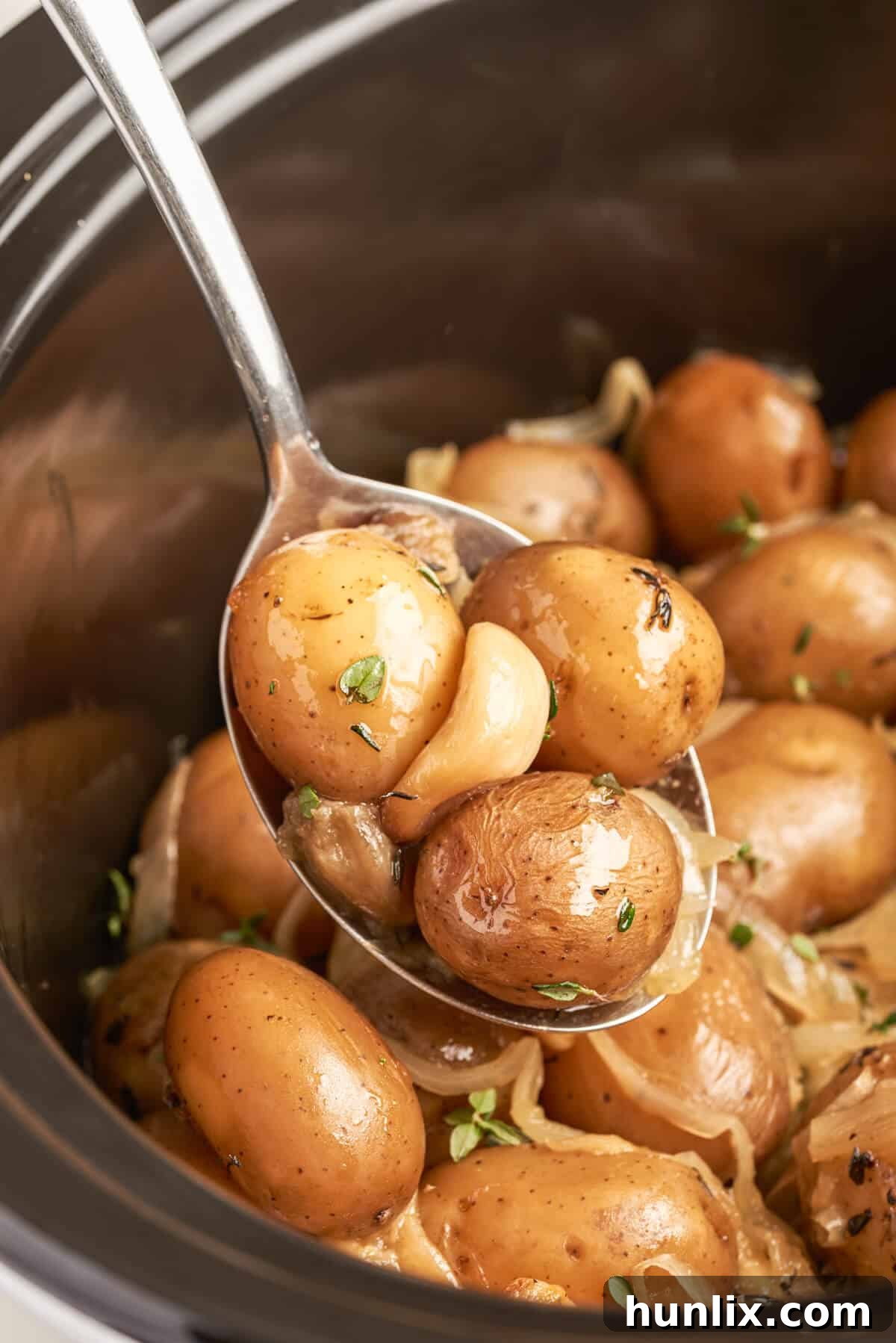 Garlic-Infused Slow Cooker Potatoes 5 A serving spoon lifting tender garlic potatoes from a slow cooker, ready to be served.