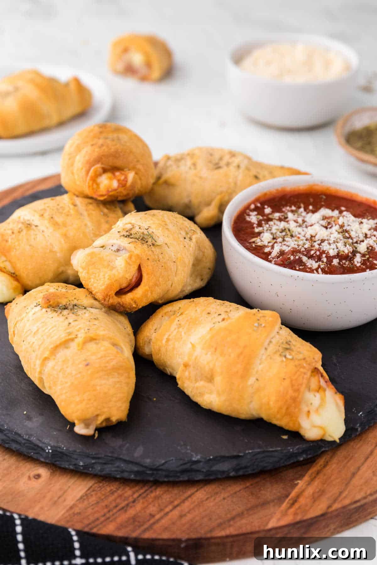 A serving of golden brown pizza rolls arranged on a stylish black round slate, highlighting their appealing texture.