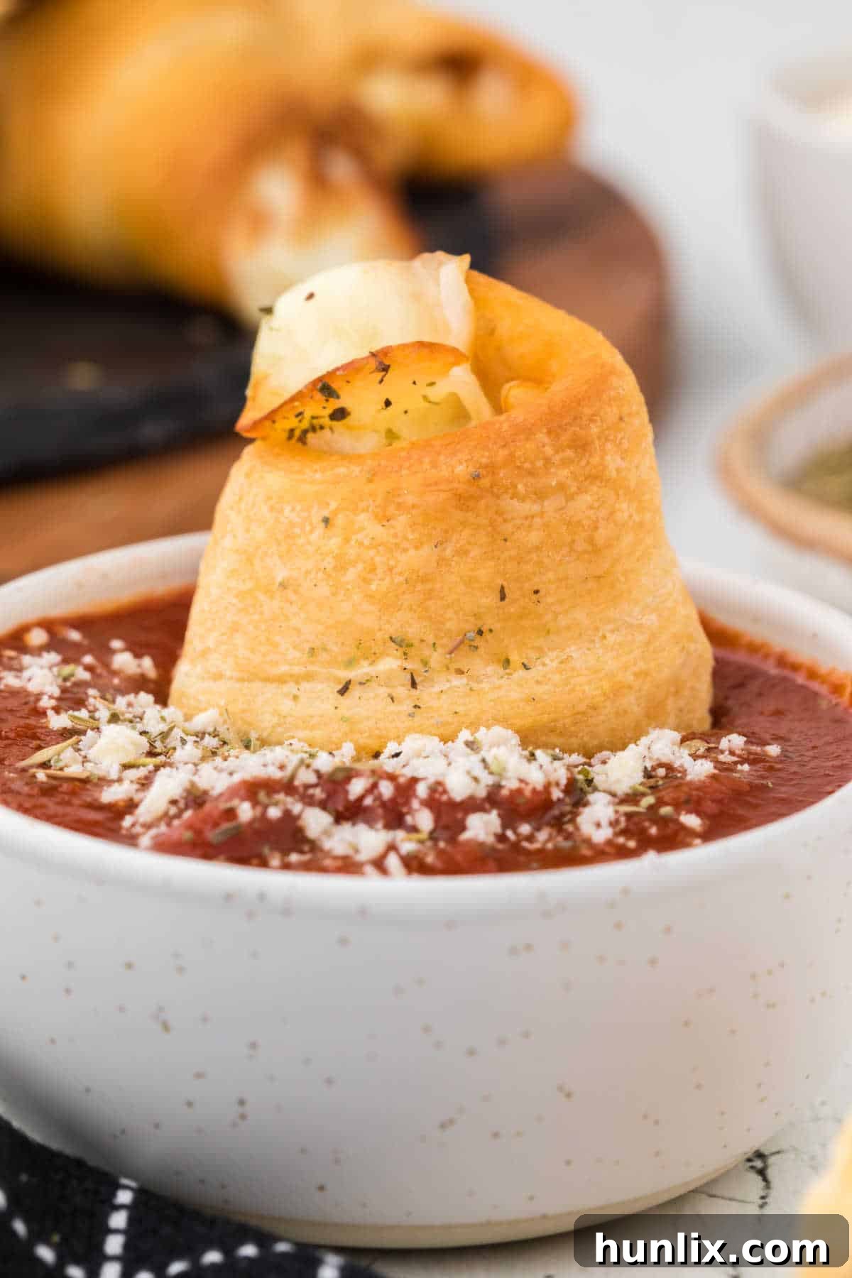 A close-up shot of a single homemade pizza roll being dipped into a bowl of rich red pizza sauce, highlighting its golden crust.