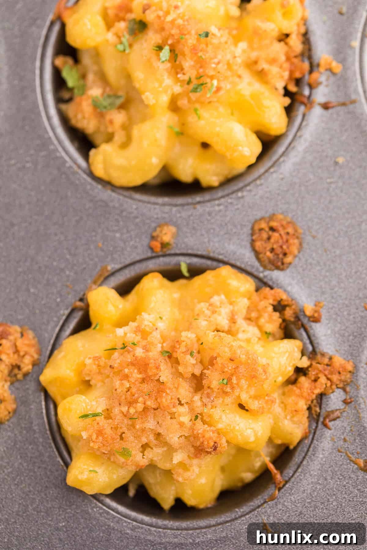 Freshly baked mac and cheese cups cooling in a muffin pan.