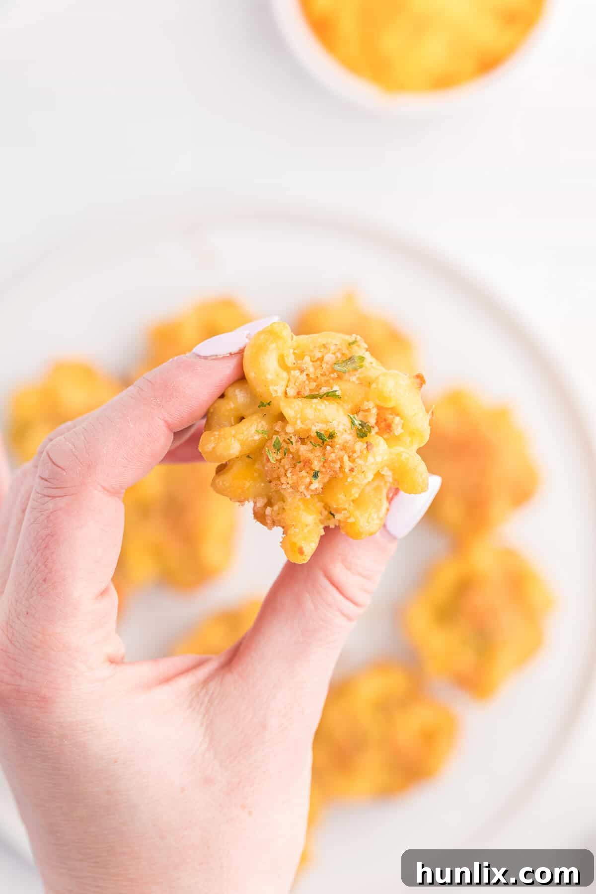 A hand holding a single mac and cheese cup with a creamy interior.