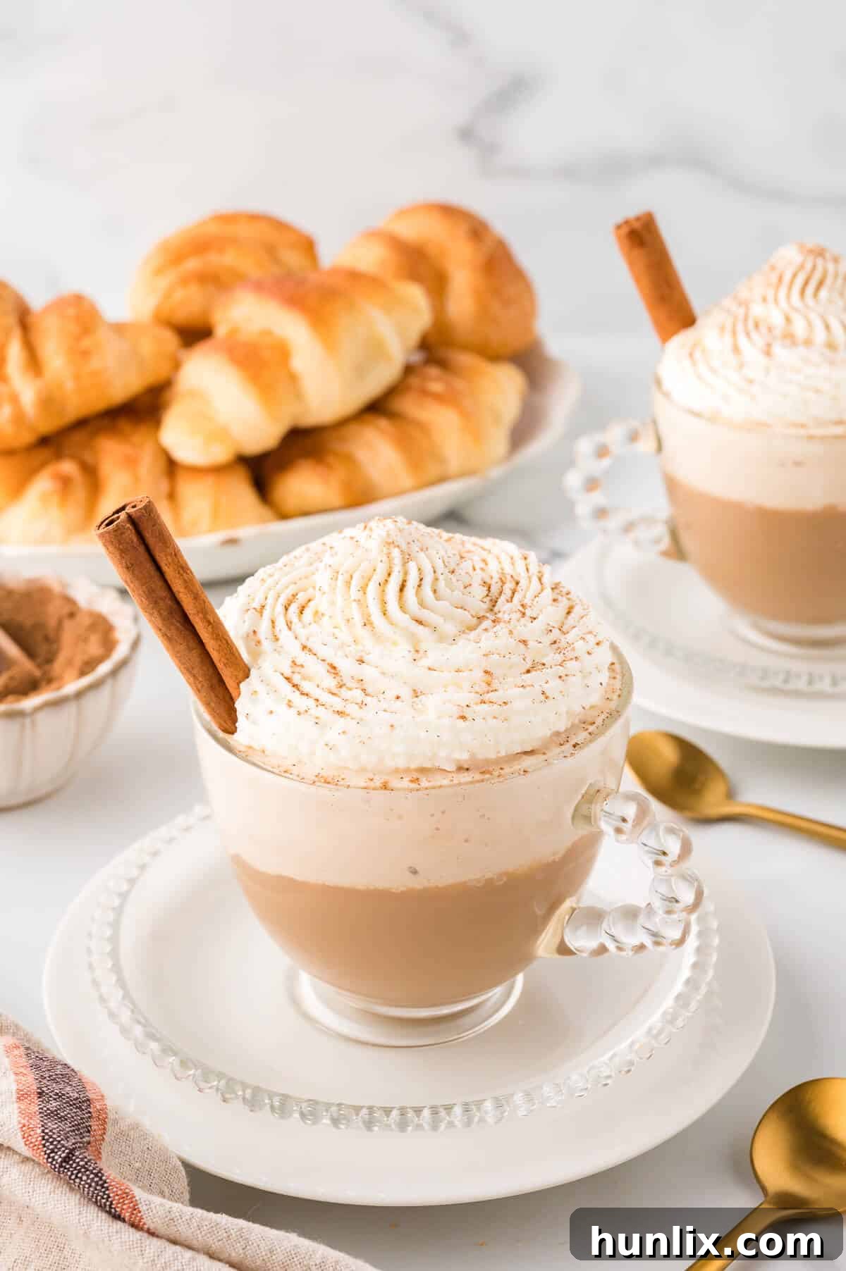 A beautifully prepared Cinnamon Cappuccino, topped with whipped cream and a sprinkle of cinnamon, served on a saucer.