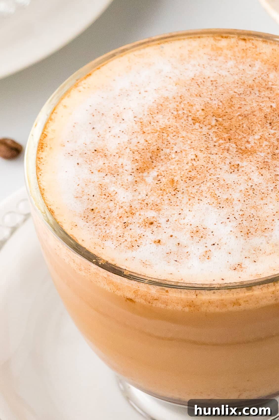 A close-up view of the frothy top of a cinnamon cappuccino mug, garnished with whipped cream and cinnamon sprinkles.