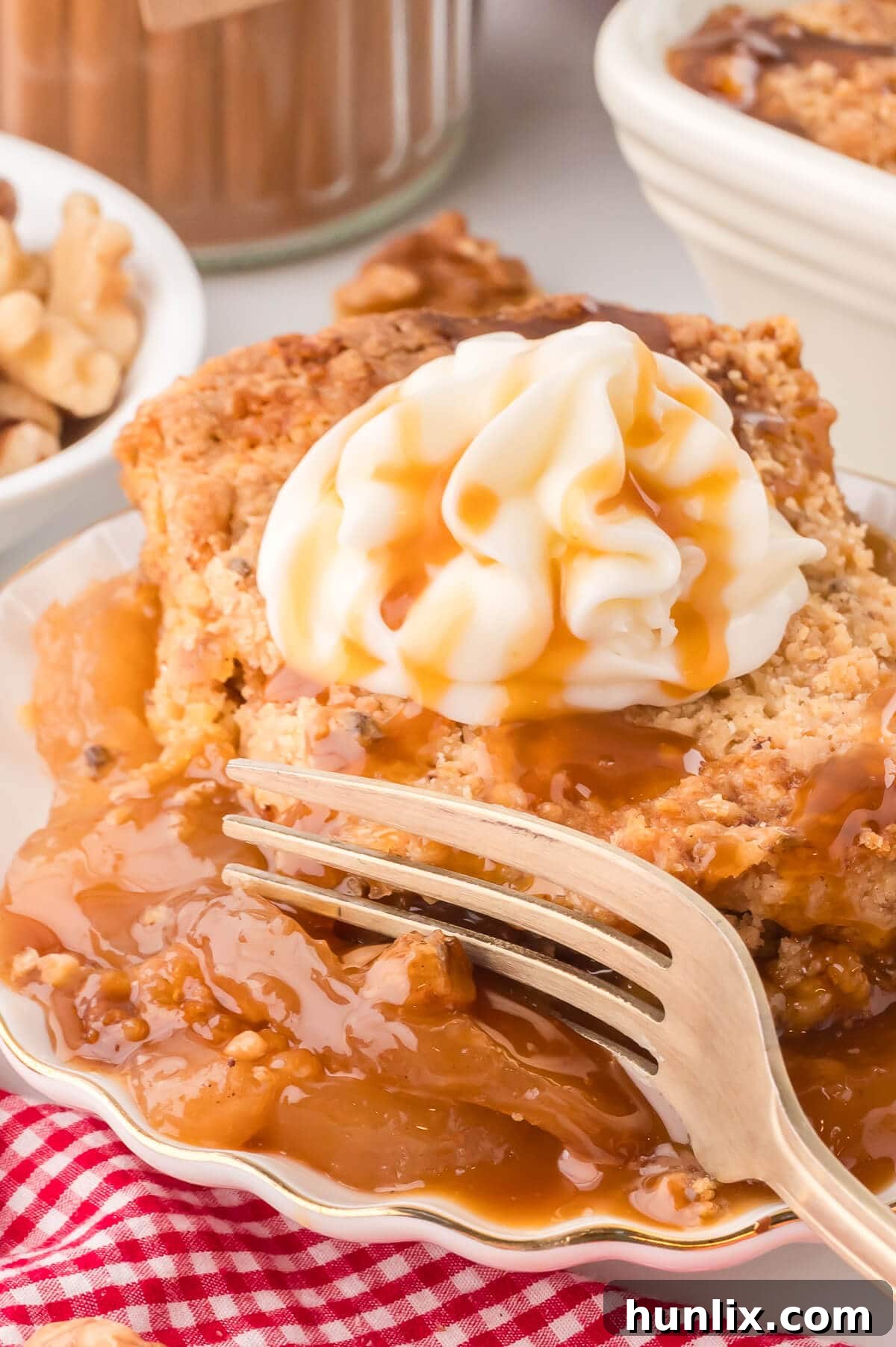 A slice of warm apple dump cake on a plate, generously topped with whipped cream and a drizzle of caramel sauce, with a fork digging in to reveal its tender interior.