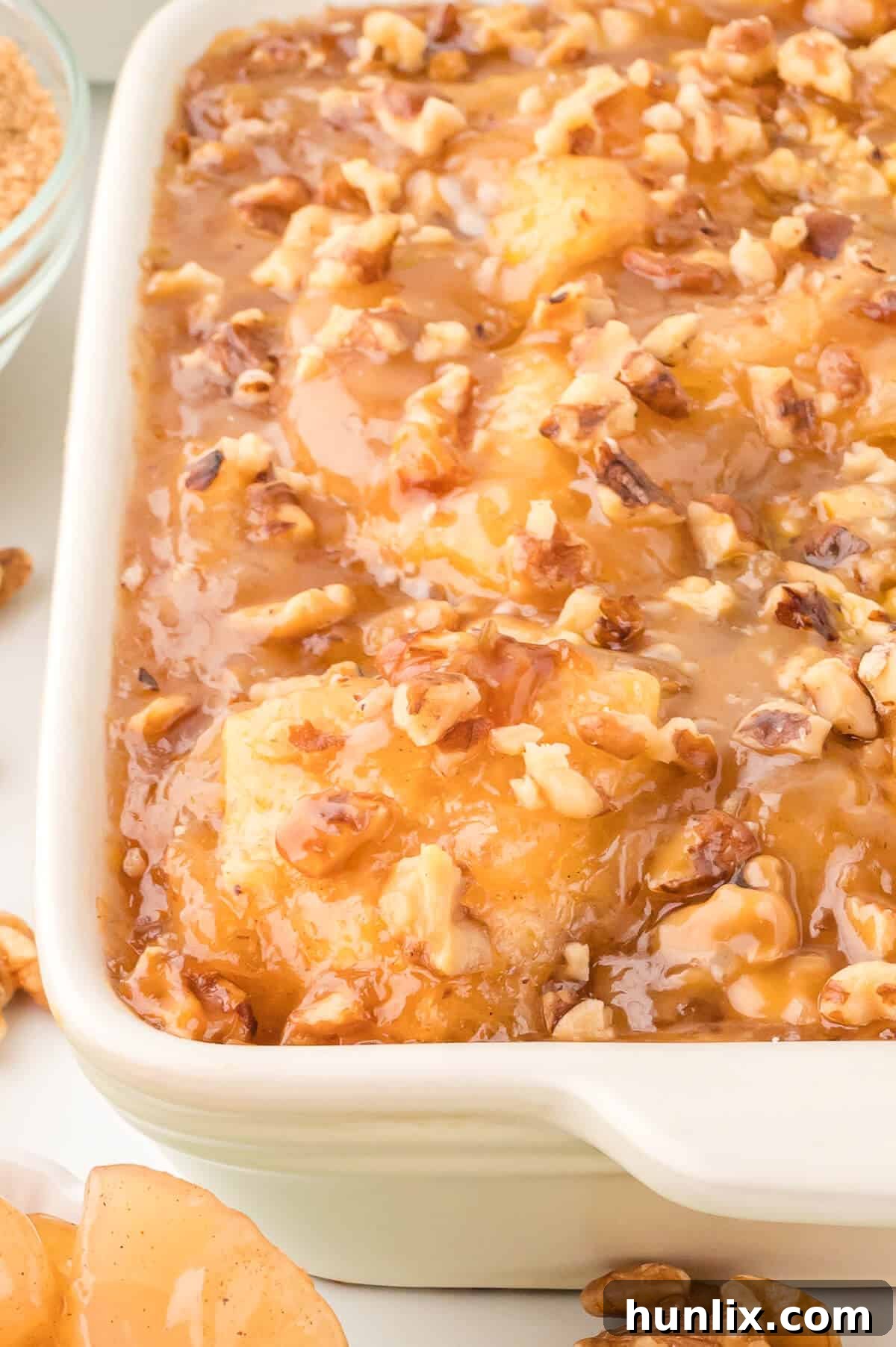 Golden-brown Apple Butterscotch Buns baking in a pan, glistening with butterscotch sauce and topped with walnuts.