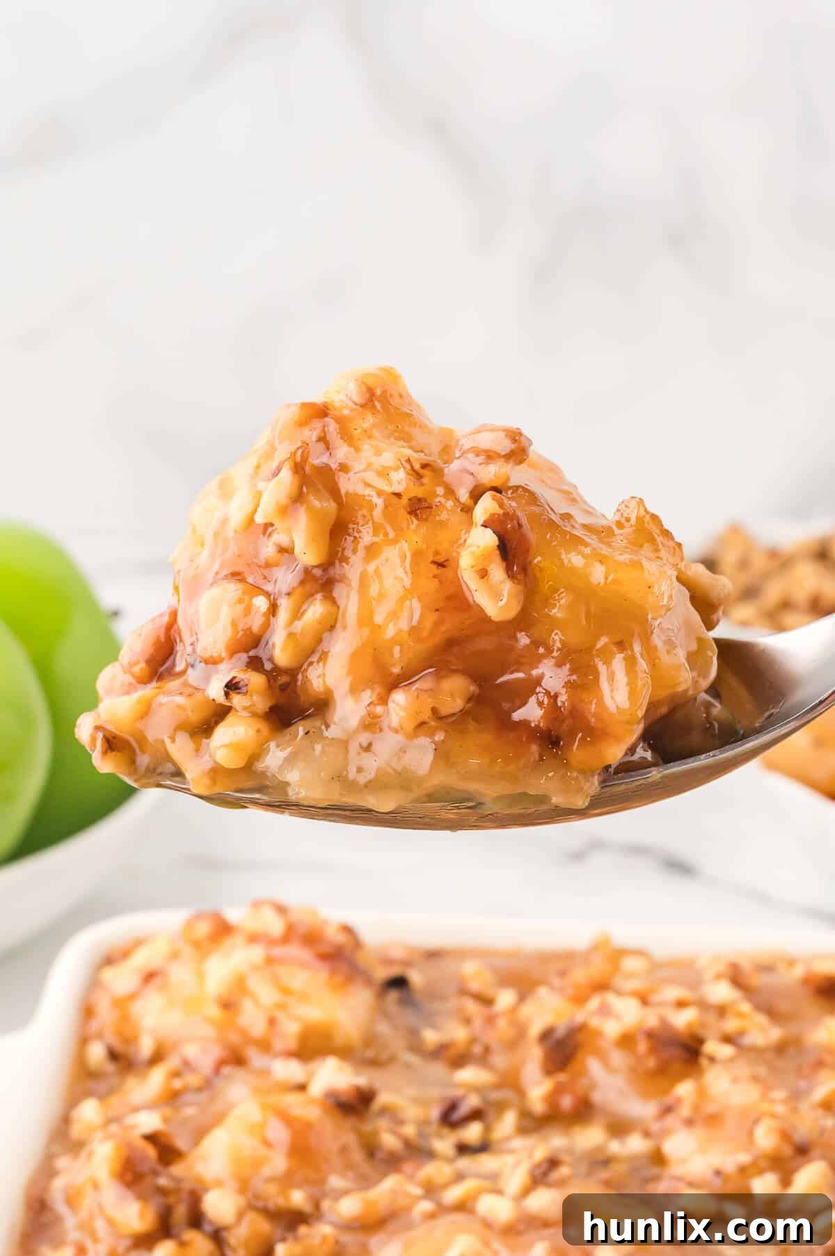 A serving spoon lifting a portion of Apple Butterscotch Buns, showing the layers of flaky dough, apple, and butterscotch.