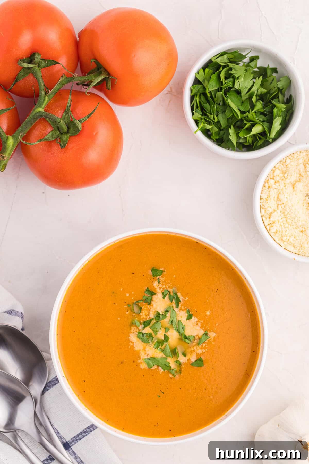 A bowl of roasted garlic and tomato soup, garnished with parmesan and herbs.
