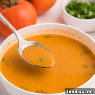 A spoon in a bowl of roasted garlic and tomato soup.