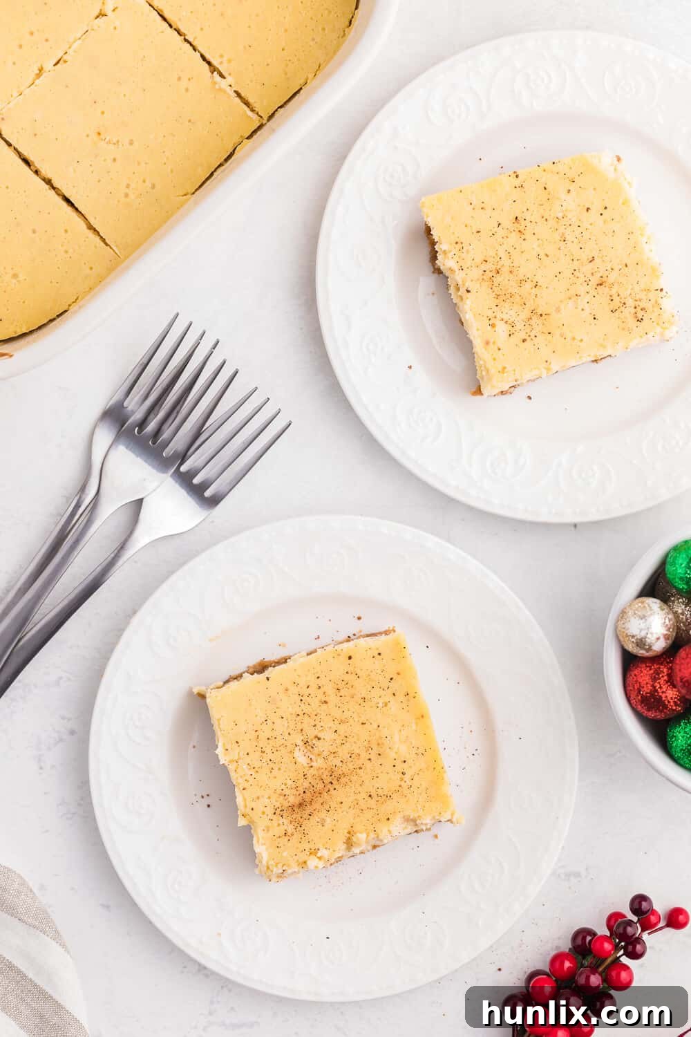 Two slices of eggnog cheesecake bars on white plates, garnished and ready to be enjoyed.