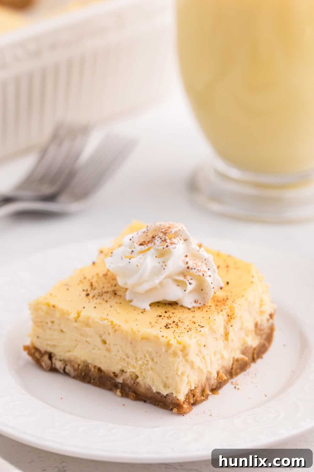 A single eggnog cheesecake bar topped with a dollop of whipped cream on a pristine white plate.