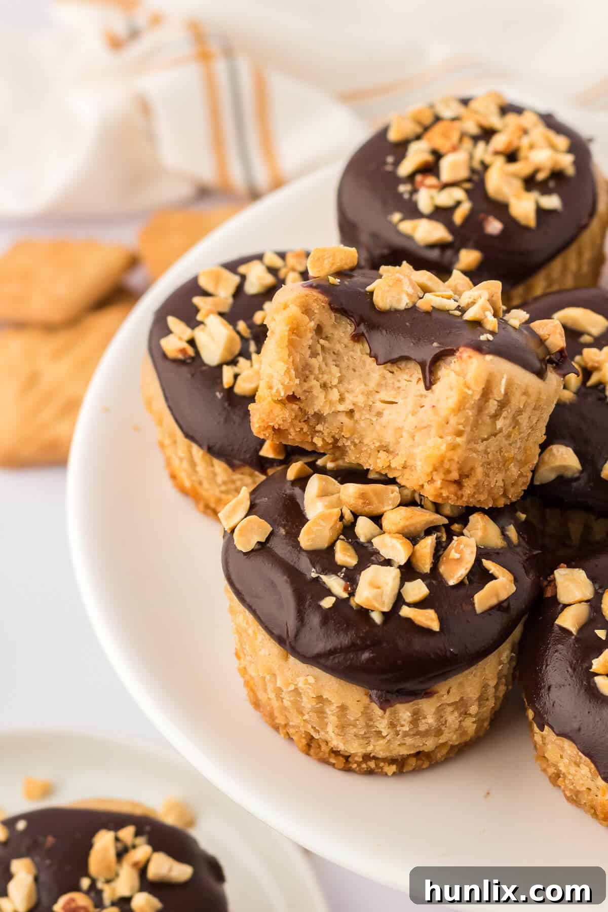 A stunning pile of mini peanut butter cheesecakes, expertly drizzled with chocolate sauce and garnished with chopped peanuts, ready to be enjoyed.