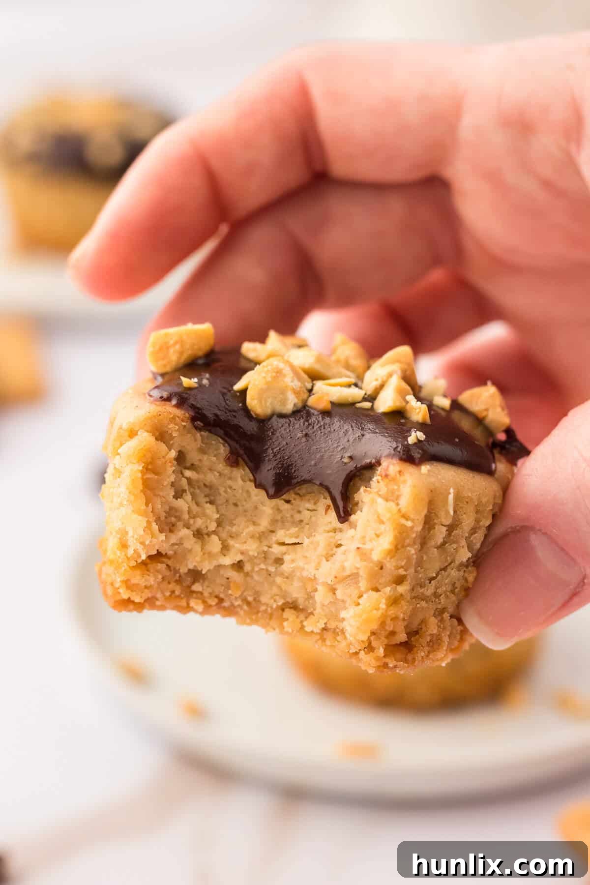 A hand holding a mini peanut butter cheesecake with a bite taken out, revealing the creamy filling and crunchy crust.