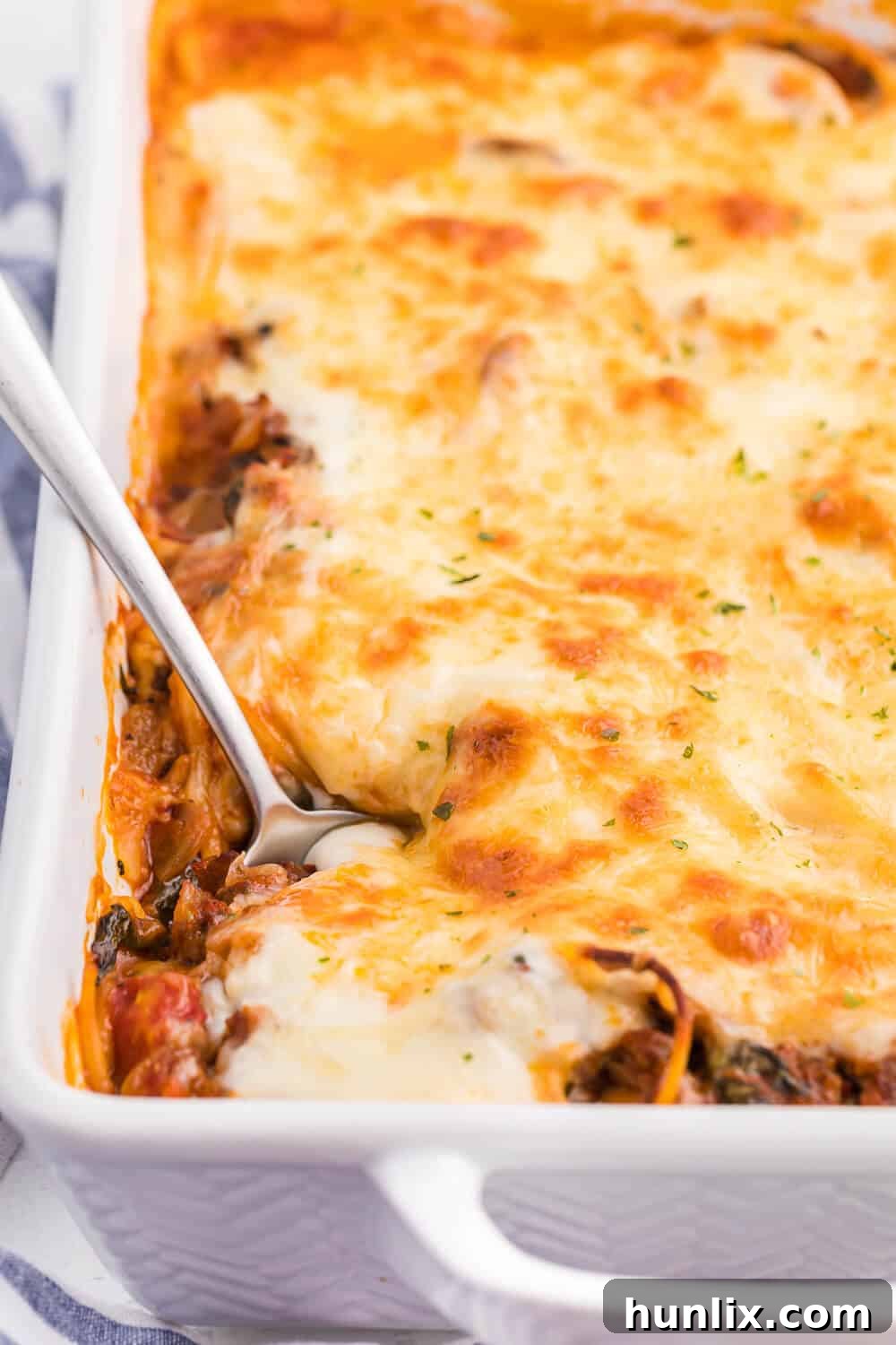 Ultimate Baked Spaghetti 2 Spaghetti bake in a white casserole pan with a serving spoon, showcasing its cheesy, saucy layers.