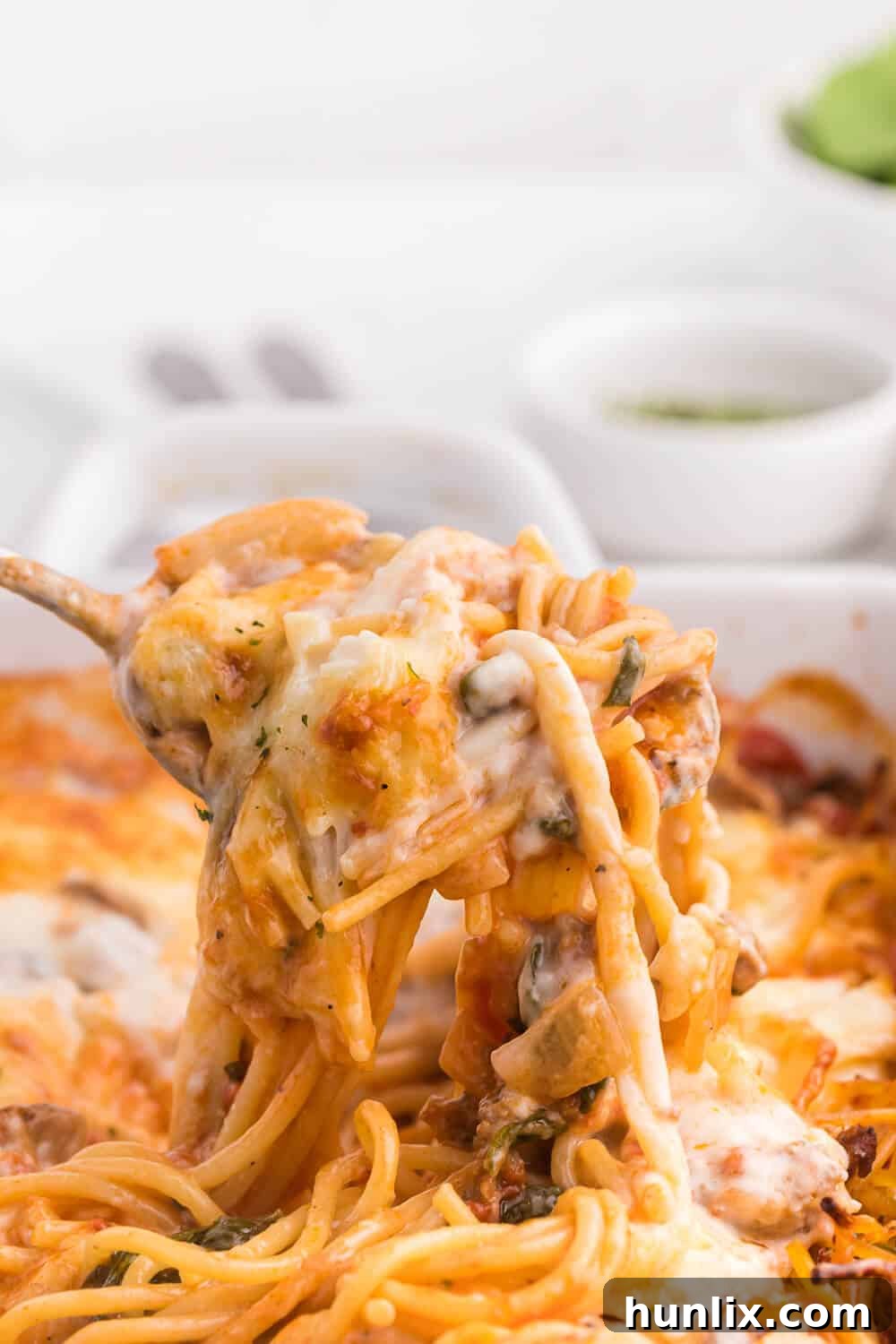 Ultimate Baked Spaghetti 4 A serving spoon lifting a scoop of spaghetti bake from a casserole dish, showing the layers of pasta, sauce, and cheese.