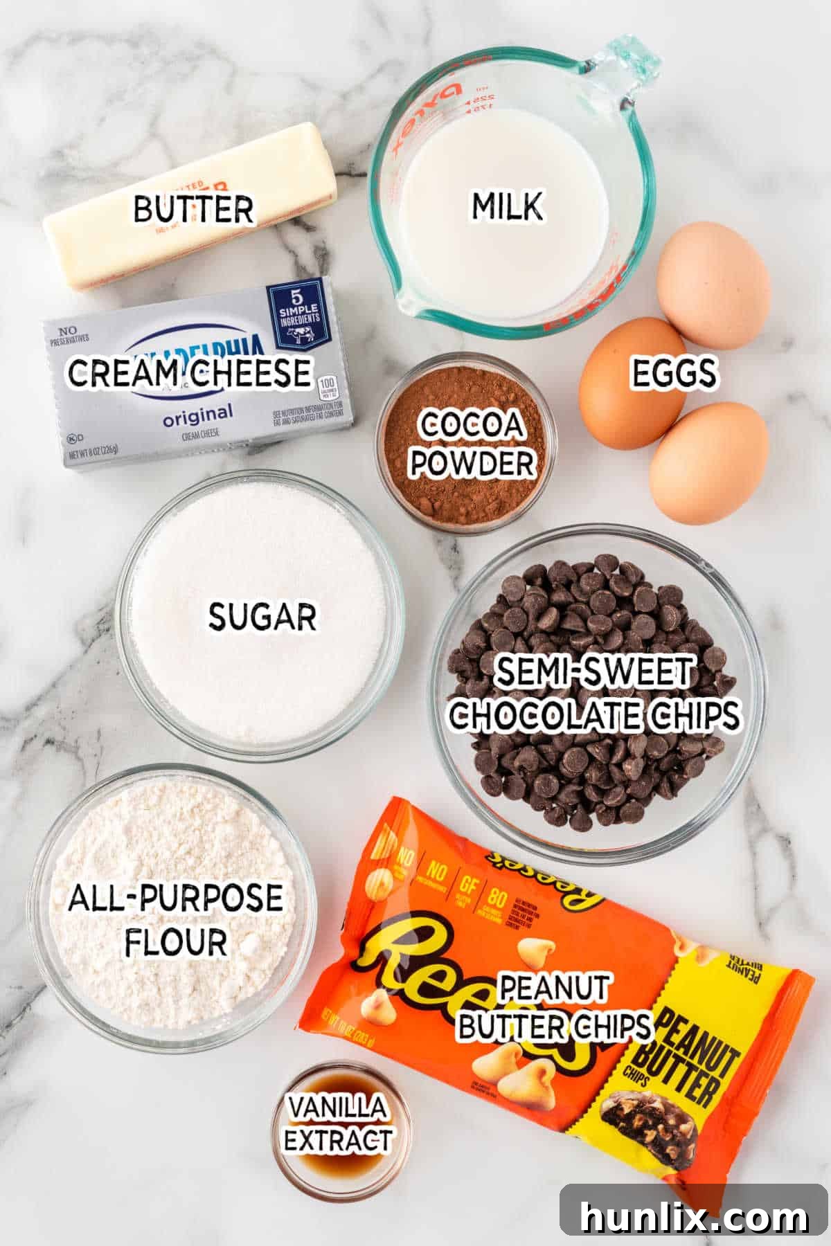 Various ingredients for peanut butter cheesecake brownies arranged on a white marble background.
