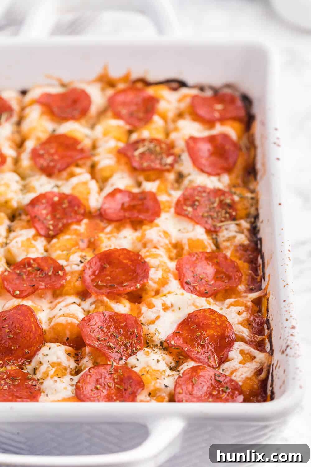 Close-up view of Pizza Tater Tot Casserole in a clean white casserole dish, showing the layers of golden tater tots, melted cheese, and hearty pizza topping mixture.