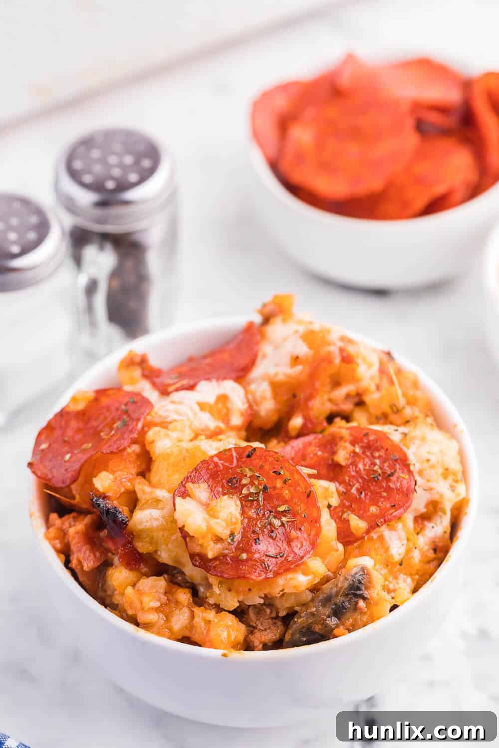 A generous serving of Pizza Tater Tot Casserole in a small white bowl, ready to be enjoyed, highlighting its comforting and hearty nature.