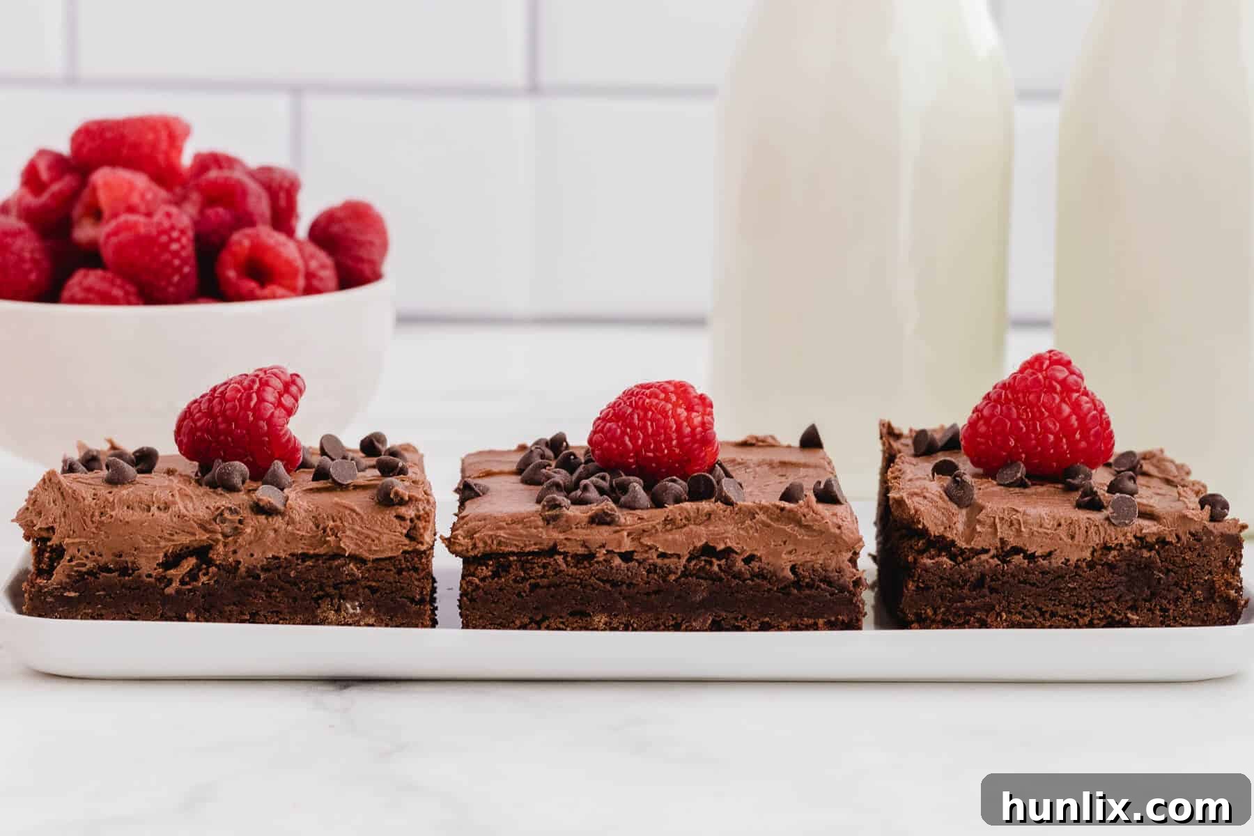 A plate featuring three perfectly portioned chocolate raspberry brownies, showcasing their rich color and creamy frosting.