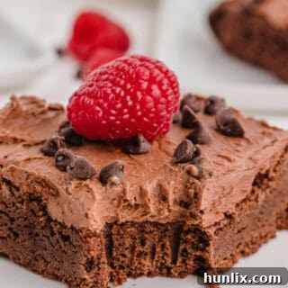 A piece of a chocolate raspberry brownie with a bite taken out, showing the fudgy interior and creamy frosting.