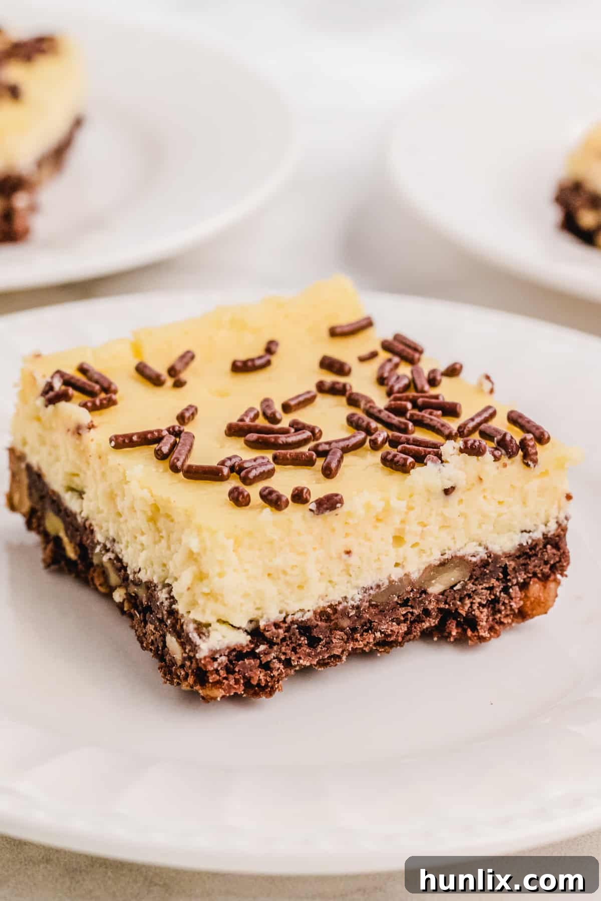 A single piece of cheesecake square, beautifully presented on a white plate.