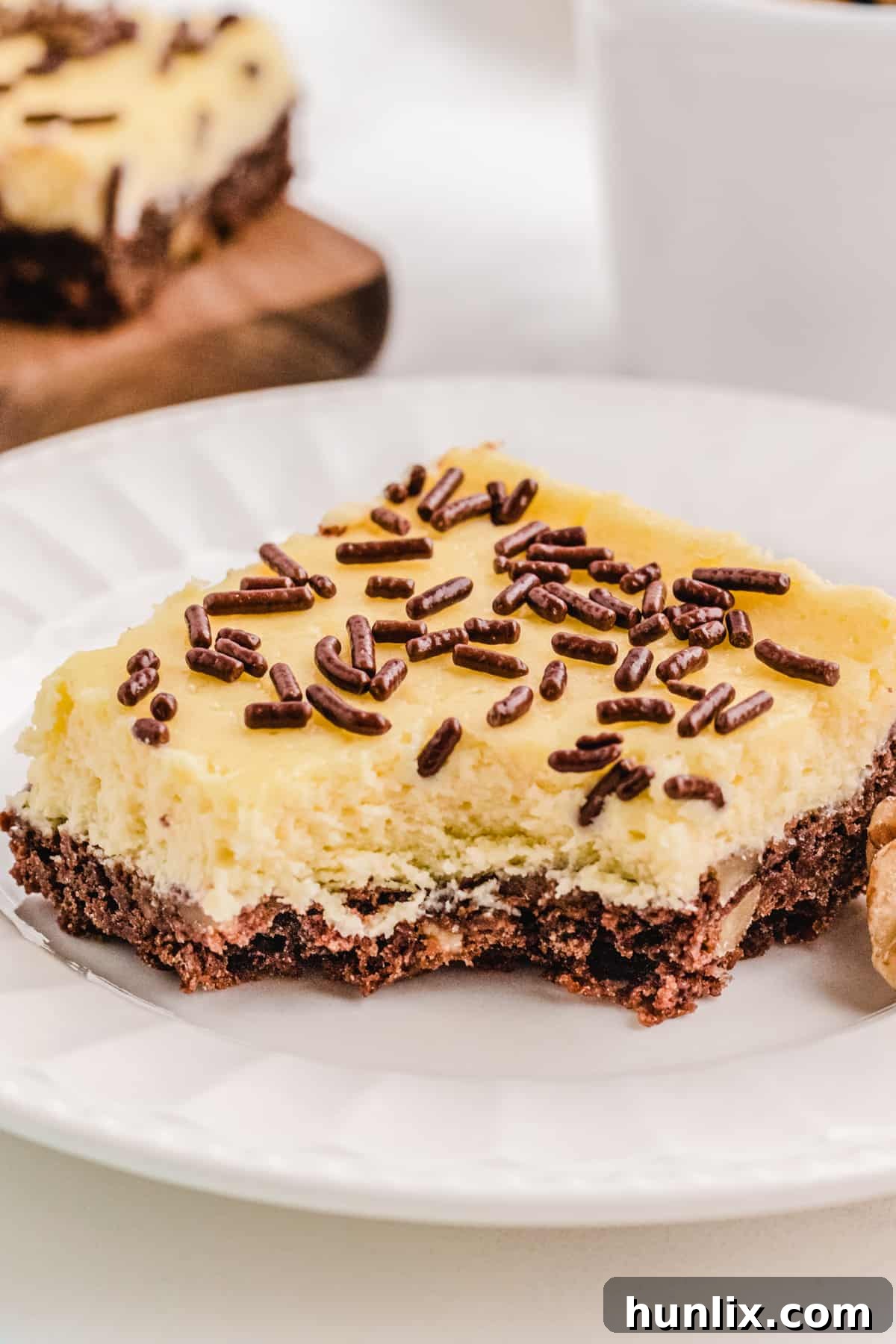 A close-up of a cheesecake square with a bite taken out, revealing the creamy interior and chocolate nut crust.