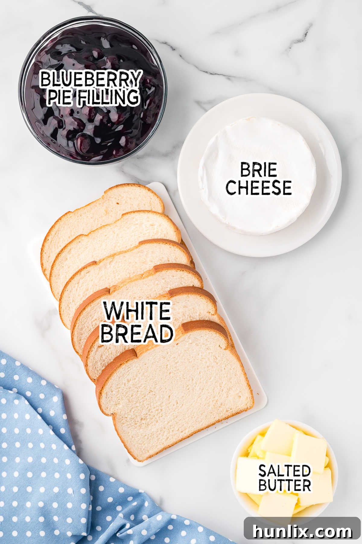 Close-up of ingredients for blueberry brie grilled cheese: bread, brie, butter, and blueberry pie filling.