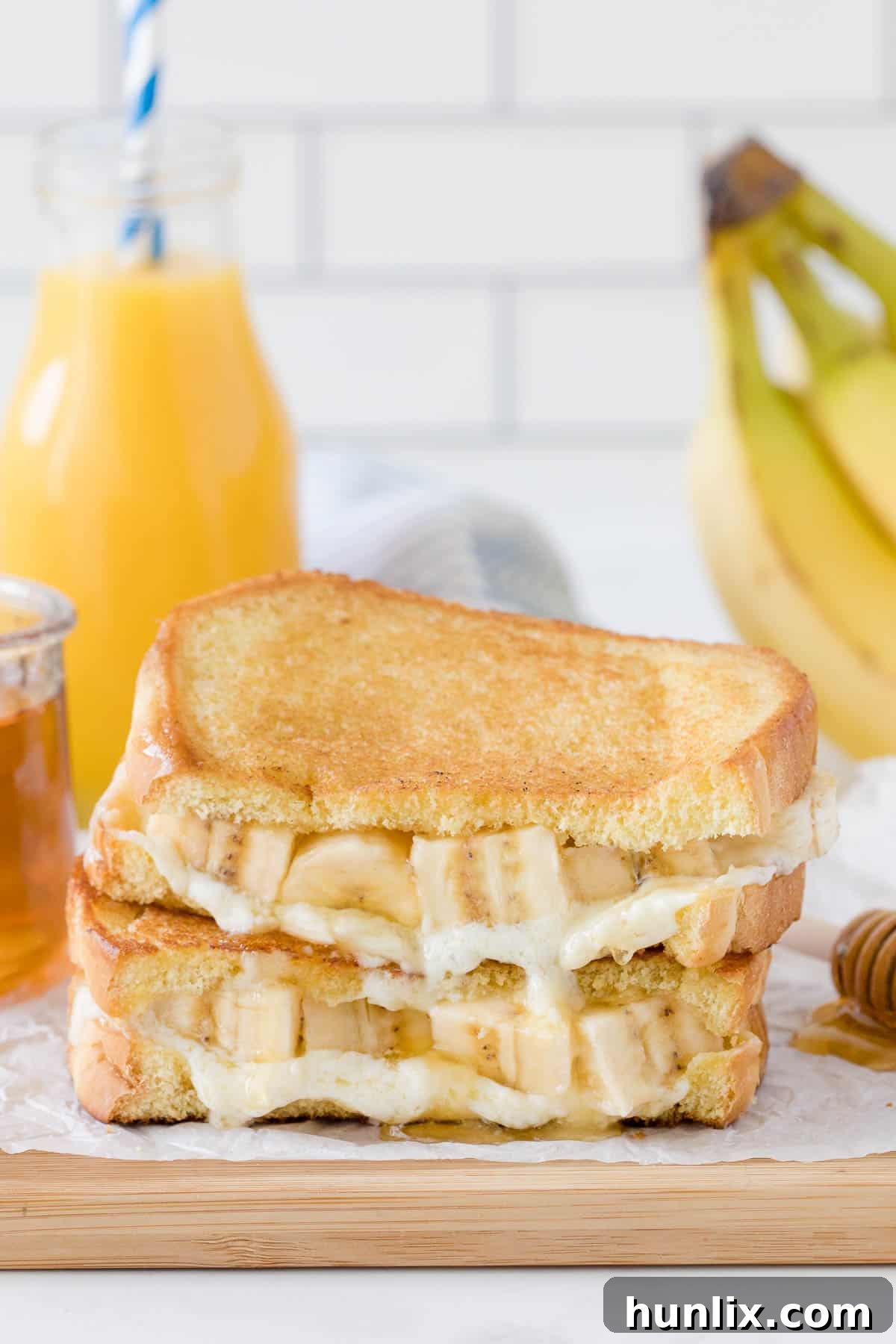Stacked Honey Banana Grilled Cheese Sandwiches on a wooden cutting board, drizzled with honey.
