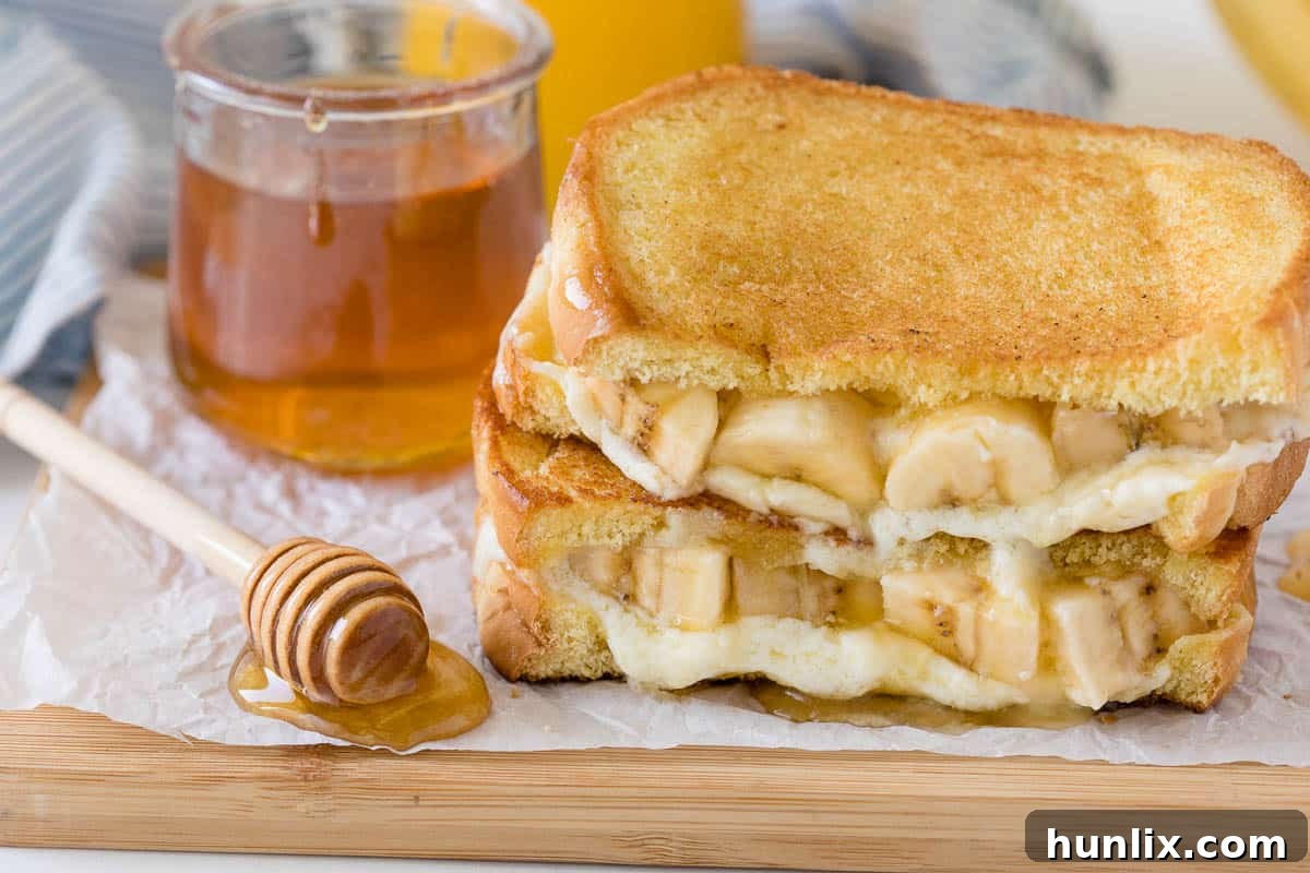 A freshly made Honey Banana Grilled Cheese on a cutting board, garnished with additional banana slices and honey.