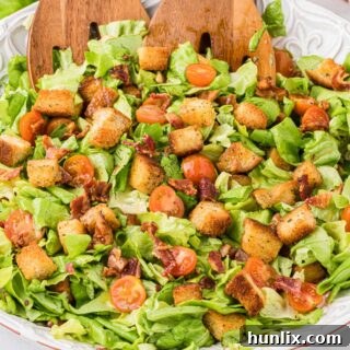 BLT salad in a bowl with wooden salad tongs.