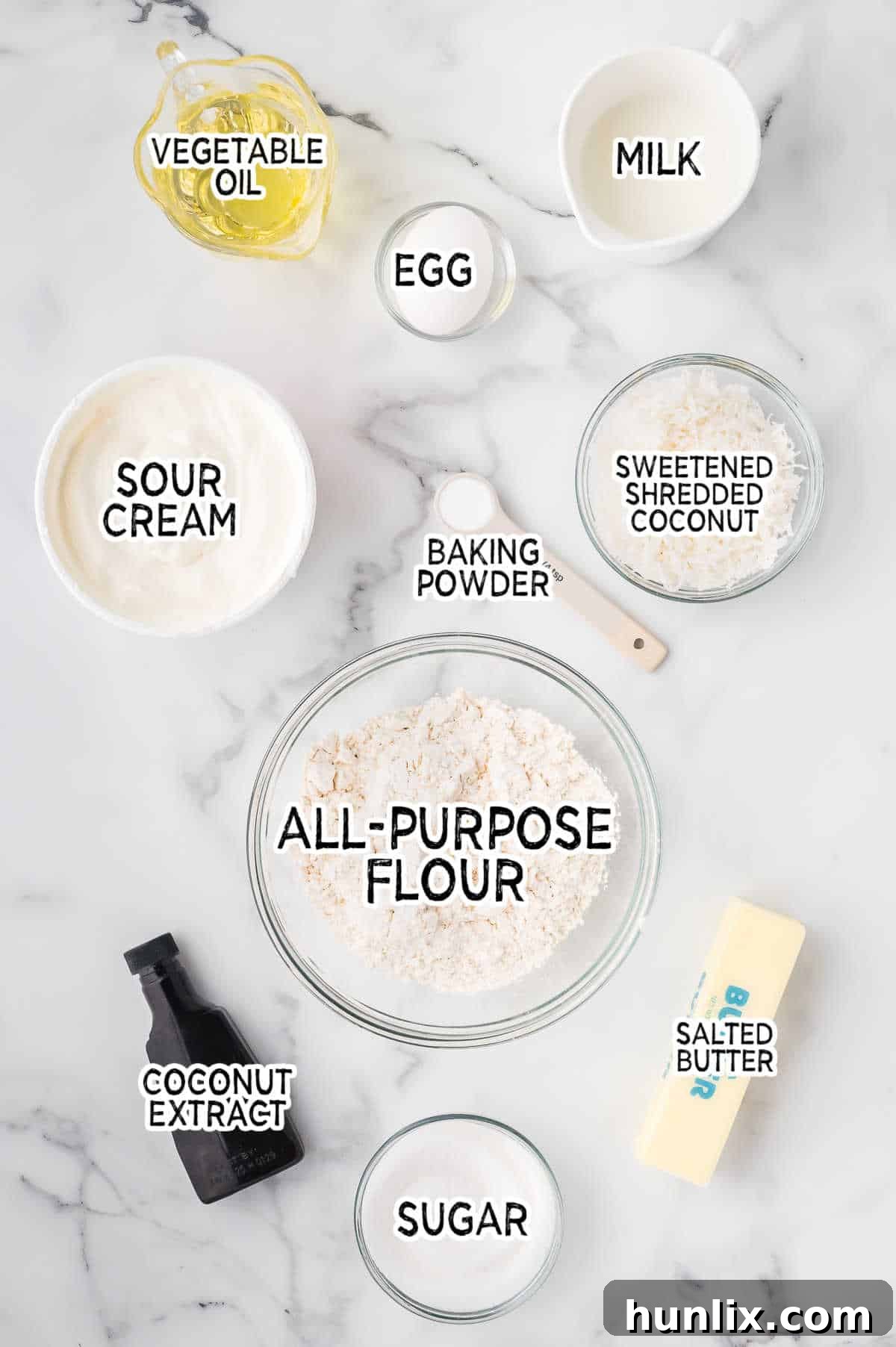 A flat lay of all the ingredients needed to bake delicious toasted coconut muffins, including flour, sugar, eggs, and shredded coconut.