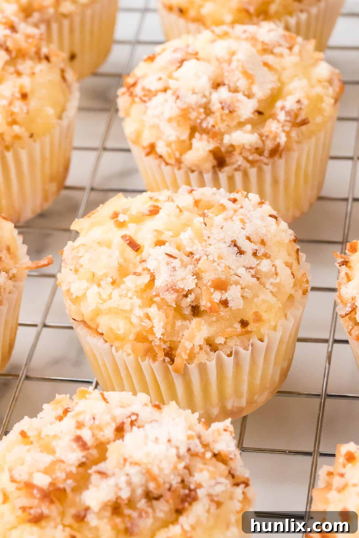 A close-up shot of several toasted coconut muffins on a wire rack, highlighting their moist interior and crispy streusel.