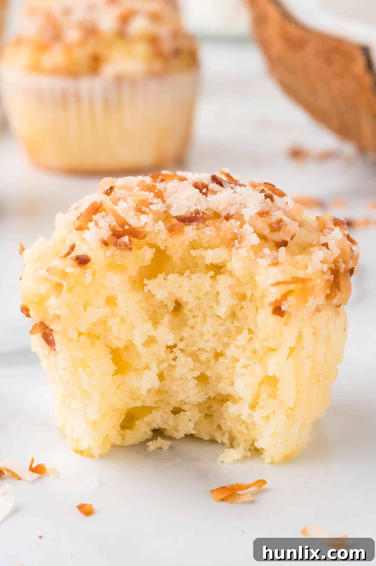 A toasted coconut muffin with a bite taken out, revealing its moist, fluffy interior.