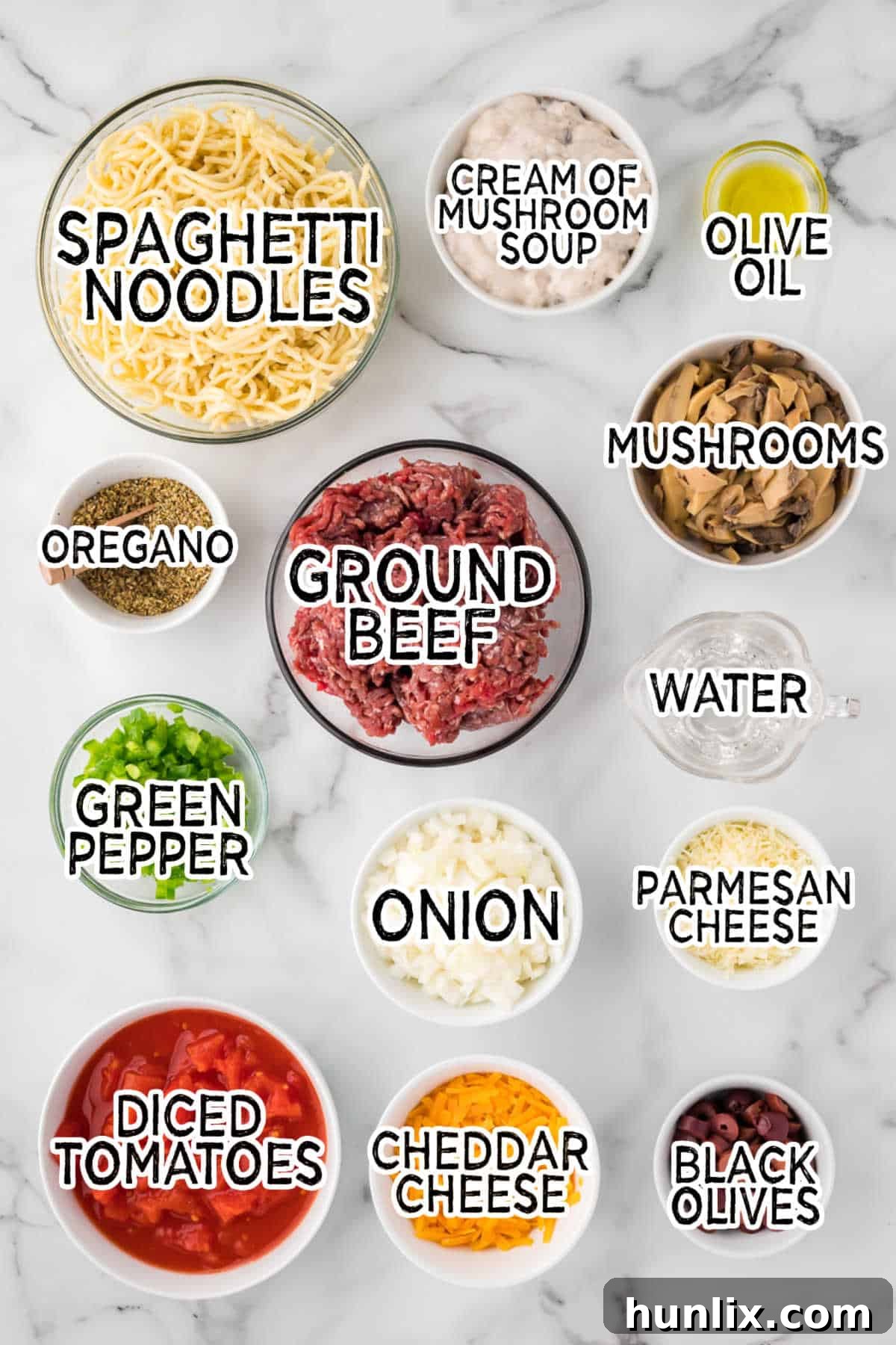 Hearty Spaghetti Bake 3 Assortment of fresh and canned ingredients for spaghetti casserole arranged on a white marble counter, including ground beef, pasta, cheese, and vegetables.