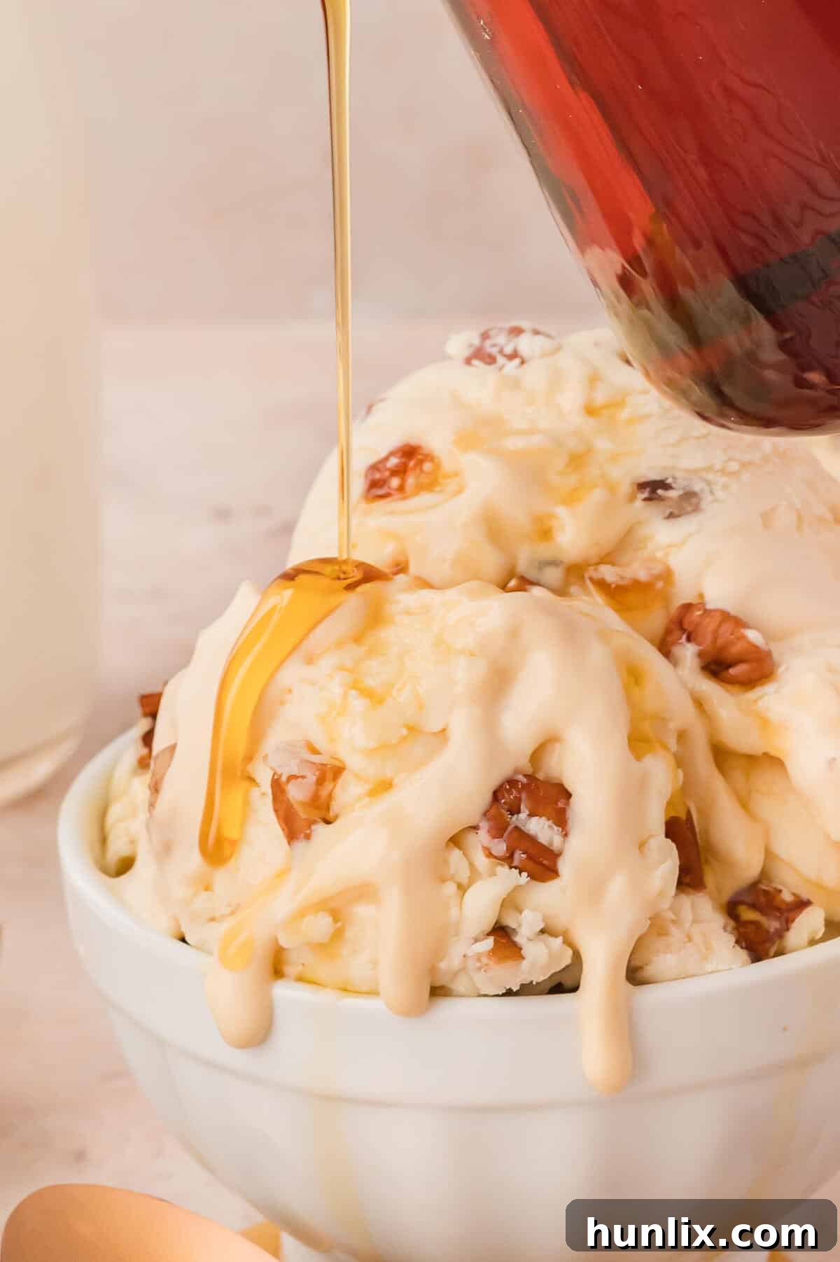 Maple Pecan Ice Cream Delight 7 Maple syrup being poured generously over a bowl of maple pecan ice cream.